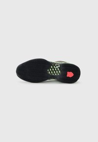 Athletic shoe sole featuring a textured black rubber surface, green mesh accents, and a red heel detail. Designed for grip and support.