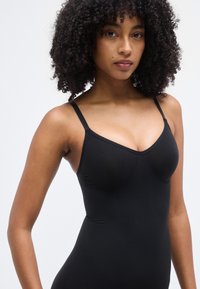 Μαύρο αμάνικο κορμάκι με ντεκολτέ σε σχήμα V. Κατασκευασμένο από λείο, ελαστικό ύφασμα. Διαθέτει λεπτές ρυθμιζόμενες τιράντες και διακριτικές λεπτομέρειες διαμόρφωσης.