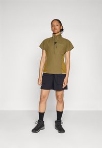 Olive green short-sleeved shirt with a partial zipper, black cargo shorts, and black hiking boots. Features contrasting side panels.