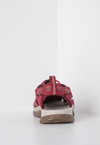 Sandalo rosso con tomaia a rete flessibile, cinturino regolabile, soletta imbottita e suola in gomma marrone chiaro, che mostra segni di usura sul fondo.