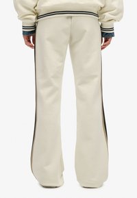 Crèmekleurige flared sweatpants van zacht materiaal, met zwarte en beige zijkanten en een geribbelde tailleband.
