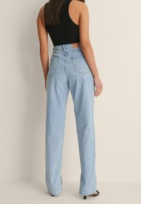 Siniset korkeat farkut suoranlahkeisella istuvuudella, joissa on takataskut, kontrastiväriset ompeleet ja lappu vyötäröllä.