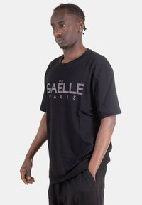 T-shirt di cotone nero con maniche corte, caratterizzato da lettering bianco in strass "GAËLLE PARIS" sul davanti, vestibilità rilassata, design semplice.