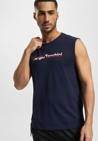 Mørkeblå ermeløs t-skjorte laget av bomull med rund hals. Har en "Sergio Tacchini" logo i rødt og hvitt over brystet.