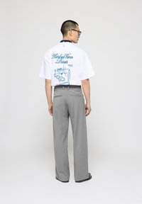 Camiseta blanca de manga corta con gráfico de "Harbor View Diner" en color azul verdoso en la parte posterior; combinada con pantalones de pierna ancha en gris claro. Fondo liso.
