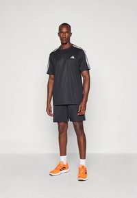 Zwart sportief T-shirt met witte strepen op de mouwen, gecombineerd met bijpassende shorts. Voorzien van oranje sportschoenen en een minimalistisch ontwerp.