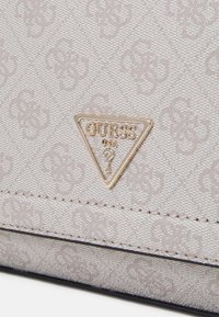 Beige fabric bag with embossed logo pattern, featuring a gold triangular logo accent and black stitching along the bottom edge.