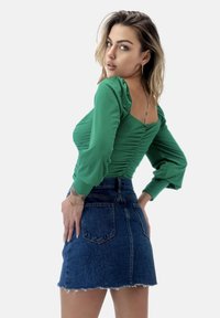 Top verde a maniche lunghe con dettagli arricciati abbinato a una mini gonna di jeans a vita alta con orlo sfilacciato e tasche posteriori.