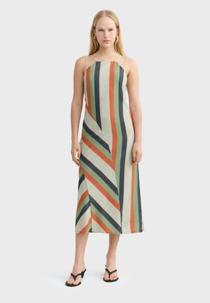 Kobieta w bezrękawowej sukience midi w zielone, pomarańczowe, granatowe i kremowe pionowe i ukośne paski, w połączeniu z czarnymi sandałami na obcasie.