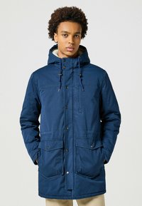 Parka azul marino con capucha, cierre de cremallera y botón, grandes bolsillos delanteros y un forro suave y texturizado. Cuenta con cuerdas ajustables.
