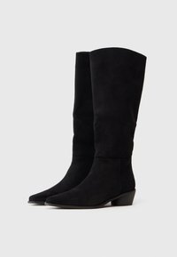 Stivali neri in suede al ginocchio con punta arrotondata, tacco basso a blocco e un design elegante e minimalista su uno sfondo semplice.