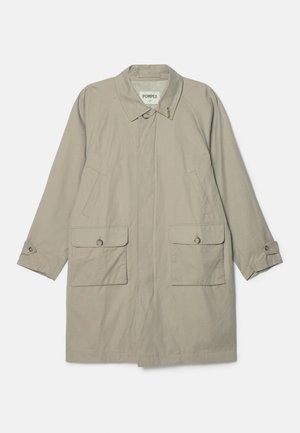 Beige trenchcoat med krageskall, to frontlommer og knappede mansjetter. Laget av et glatt, slitesterkt stoff.