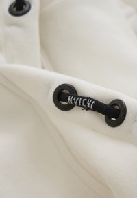 Tissu blanc mettant en valeur un cordon de serrage noir et des œillets noirs. La texture semble douce, avec des coutures visibles le long des bords.