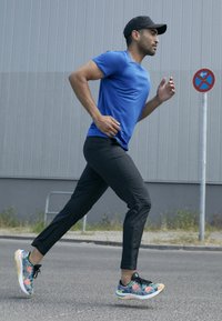 L'abbigliamento da corsa include una maglia blu a maniche corte, pantaloni neri a gamba stretta e sneaker colorate con motivi floreali.