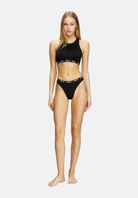 Ensemble de vêtements de sport noir comprenant un crop top sans manches avec une bande de marque et un string taille haute avec une ceinture élastique assortie.