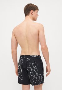 Menns svarte svømmedrakter med et hvitt abstrakt mønster, elastisk midje og baklomme. Designet for komfort og vannaktiviteter.