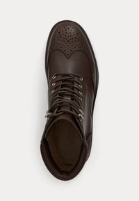 Ruskeat nahkasaappaat, joissa on brogue-tyyliset yksityiskohdat, pyöreä kärki, kuusi reikää nauhoille ja tummanvihreät nauhat; sileä pinta, jossa on voimakkaat ompeluakkentit.