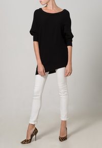 Maglione nero lavorato a maglia con scollo ampio e dettagli in perline, abbinato a jeans skinny bianchi e tacchi alti con stampa leopardata.