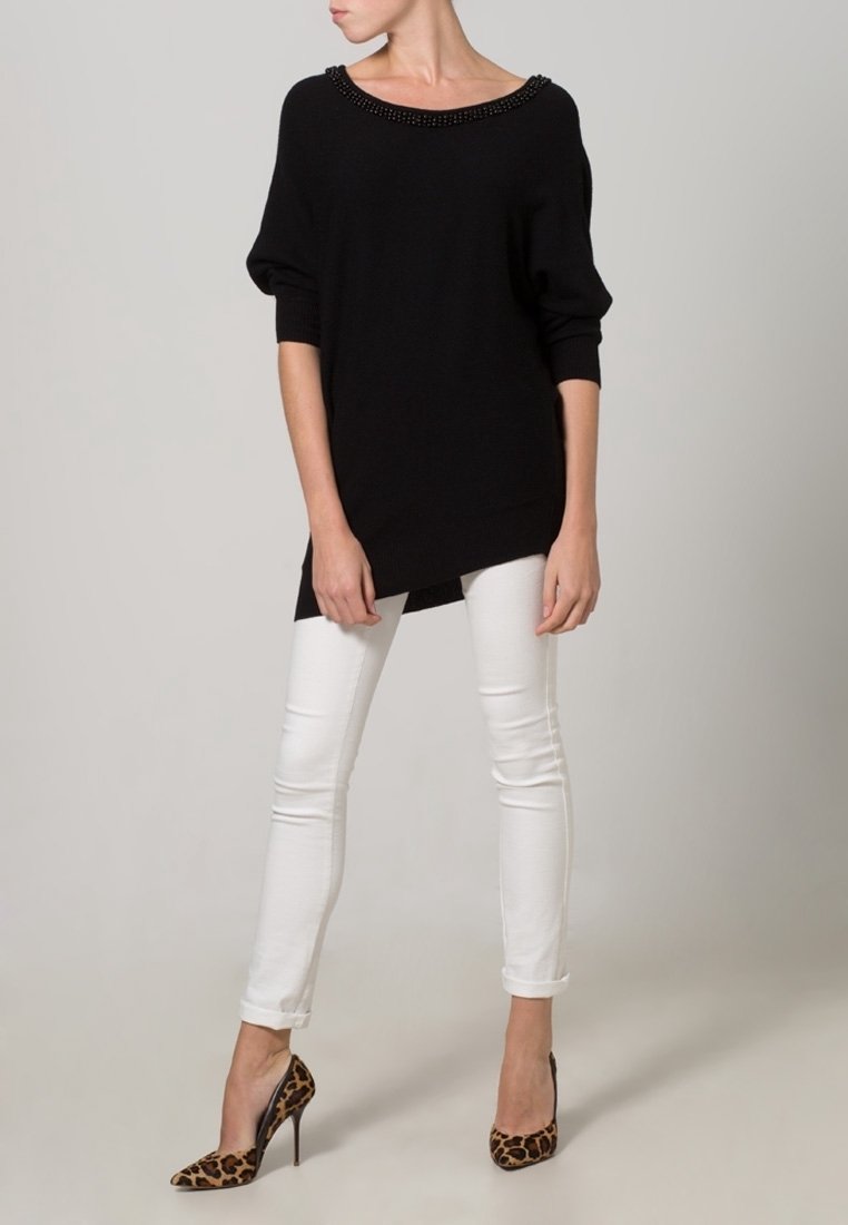 Maglione nero lavorato a maglia con scollo ampio e dettagli in perline, abbinato a jeans skinny bianchi e tacchi alti con stampa leopardata.