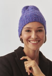 Kootud lilla beanie, millel on tekstureeritud viimistlus. Omab kitsenevat ülaosa ja juhuslikku, lõõgastavat sobivust. Pehme materjal sobib külmade ilmade jaoks.