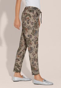 Blumenmuster-Hosen aus leichtem Material in Beige mit grünen und orangenen Akzenten, ausgestattet mit einem elastischen Bund und einem Kordelzug für eine verstellbare Passform.