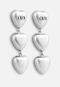 Srebrne kolczyki w kształcie serca z trzema ułożonymi w stos sercami, o wypolerowanej powierzchni, połączone metalowymi akcentami, z logo marki na górnym sercu.