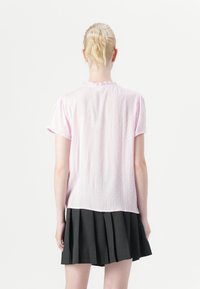 Blusa rosa a maniche corte con un sottile motivo testurizzato e scollo arricciato, abbinata a una gonne plissettata nera.