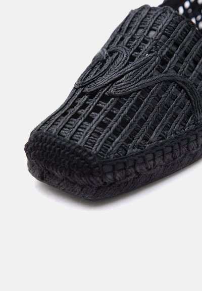 Orteil de sandale tissée noire avec des brides tressées et une semelle cousue sur fond blanc.