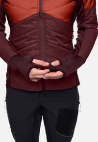 Giacca isolante bordeaux con un design geometrico in diverse tonalità, caratterizzata da aperture per il pollice e dettagli in tessuto testurizzato sulle maniche.