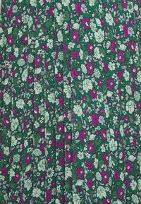 Blumiges Plissée-Kleid mit grünem Hintergrund, auf dem lila und hellgrüne Blumen und Blätter abgebildet sind. Der Stoff wirkt leicht und hat eine weiche Textur.