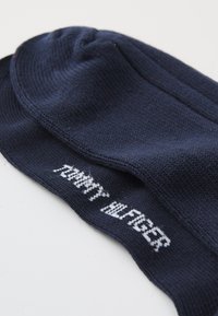 Chaussettes en coton bleu marine avec une texture côtelée et un logo "TOMMY HILFIGER" blanc le long de la cheville. Forme standard, conçues pour un usage quotidien.