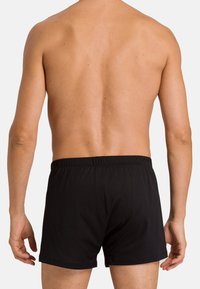 Boxer shorts de algodón negro con una cintura elástica, vistas desde atrás. Textura suave, diseño simple y sin patrones ni acentos.