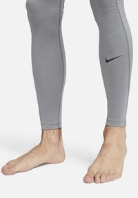 Grå treningstights laget av stretchstoff, med en tettsittende design, flate sømmer og en liten svart Nike-logo på venstre bein.