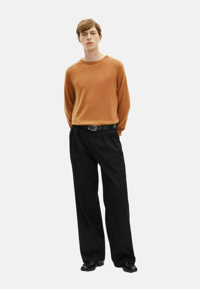 Pull en maille texturée marron avec col rond, associé à un pantalon plissé noir et des chaussures noires, muni d'une ceinture noire.