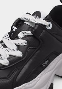 Μαύρο δερμάτινο αθλητικό παπούτσι με παχιά λευκή σόλα, κορδόνια με λευκό και μαύρο μοτίβο, και ετικέτα με την επωνυμία «Buffalo» στο πλευρικό πάνελ.