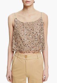 Beige paljetter crop top med tunna justerbara band; har en lös passform och ett något genomskinligt överdrag. Matchad med högmidjade beige byxor.