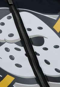 Details des Neoprenanzugs mit einem schwarzen Metallreißverschluss, weißem Stoff und einem cartoonhaften grafischen Design in Grautönen und Schwarz.