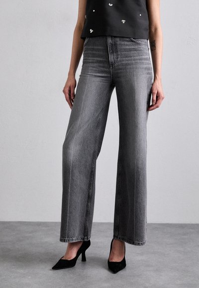 Jeans grii cu croi larg, prezentând o spălare decolorată, talie înaltă și buzunare frontale, asortați cu pantofi cu vârf ascuțit negri.