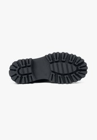Czarny gumowy outsole z solidnym wzorem bieżnika, z głębokimi rowkami zapewniającymi przyczepność oraz gładką centralną częścią dla elastyczności.