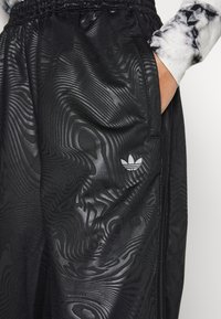 Svarta träningsbyxor med ett texturerat, vågigt mönster. Har ett elastiskt midjeband och en liten vit logotyp på sidan.