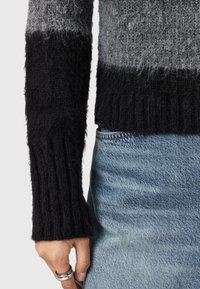 Maglione a maglia con strisce sfumate in grigio e nero. Le maniche sono a coste, realizzate in materiale morbido e peloso, abbinate a jeans in denim blu chiaro.