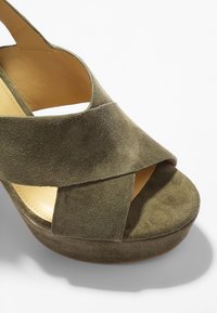 Sandale à plateforme en daim vert olive avec des sangles croisées et un bout ouvert, montrant une doublure intérieure beige lisse.