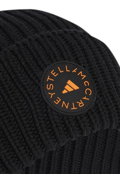 Melna adīta beanie cepure ar ribotu tekstūru, ar apaļu uzšuvi, kurā ir oranžs logotips un akcenti. Mīksts, silts materiāls.
