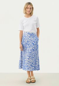 Fustă maxi cu model alb și albastru, cu croială lejeră și buzunare laterale, asortată cu un tricou alb simplu. Sandalele completează ținuta.