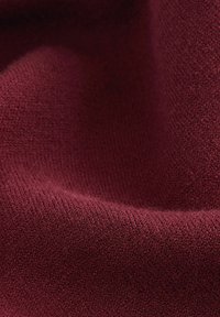 Gros plan d'un tissu bordeaux plié et texturé avec des fibres tissées douces et une ombre subtile.