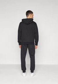 Sudadera con capucha negra y pantalones de chándal a juego, hechos de una tela suave, con puños y cintura elásticos, combinados con zapatillas deportivas blancas.