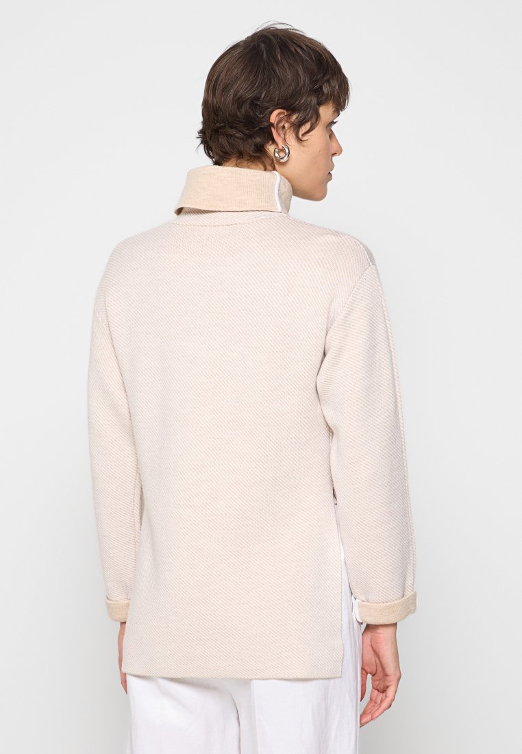 Beiger Pullover mit einem strukturierten Muster, hohem Kragen und umgeschlagenen Bündchen. Hat einen geraden Schnitt und einen leicht längeren Rücken.