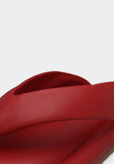 Zbliżenie na czerwoną, wyściełaną klapkę na ślizgu z szerokim paskiem o gładkiej teksturze na białym tle.