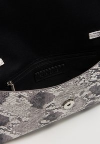 Sac à main en simili cuir gris avec un extérieur lisse et texturé. L'intérieur présente une doublure en tissu noir et une poche zippée pour le rangement.