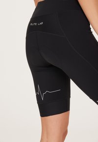 Zwarte fietsbroek van rekbare stof. Kenmerken zijn onder andere een grafisch hartslaglijn, een contrasterend logo op de waistband en een naadloos ontwerp.